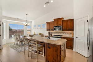 Kitchen featuring vaulted ceiling, light stone countertops, decorative backsplash, stainless steel appliances, and a kitchen island with sink