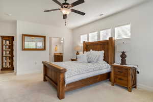 Bedroom with light colored carpet, multiple windows, a ceiling fan, and ensuite bath
