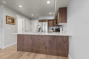 Kitchen with light wood-style flooring, stainless steel fridge, a peninsula, light stone counters, and recessed lighting