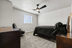 Bedroom featuring light colored carpet, ceiling fan, a desk, and a textured ceiling