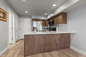 Kitchen with wood tiled floors, a peninsula, stainless steel appliances, recessed lighting, and light stone counters