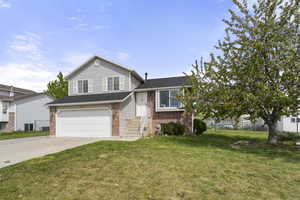 Split level home with concrete driveway, a garage, brick siding, and a front yard