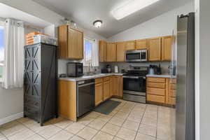 Kitchen featuring stainless steel appliances, light countertops, lofted ceiling, and light tile patterned floors