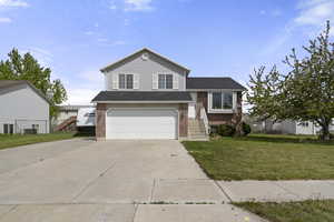 Tri-level home with a front yard, driveway, brick siding, an attached garage, and roof with shingles