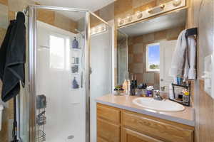 Bathroom featuring a stall shower, vanity, healthy amount of natural light, and tile walls