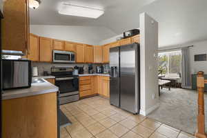Kitchen with stainless steel appliances, light colored carpet, light countertops, vaulted ceiling, and light tile patterned floors