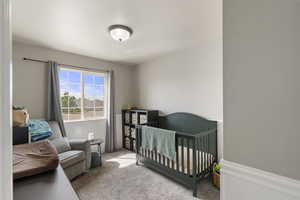 Bedroom featuring a nursery area, wainscoting, and light carpet