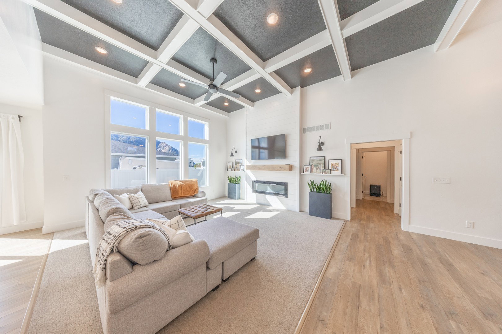 Living room with light wood-style floors, coffered ceiling, a large fireplace, and a ceiling fan
