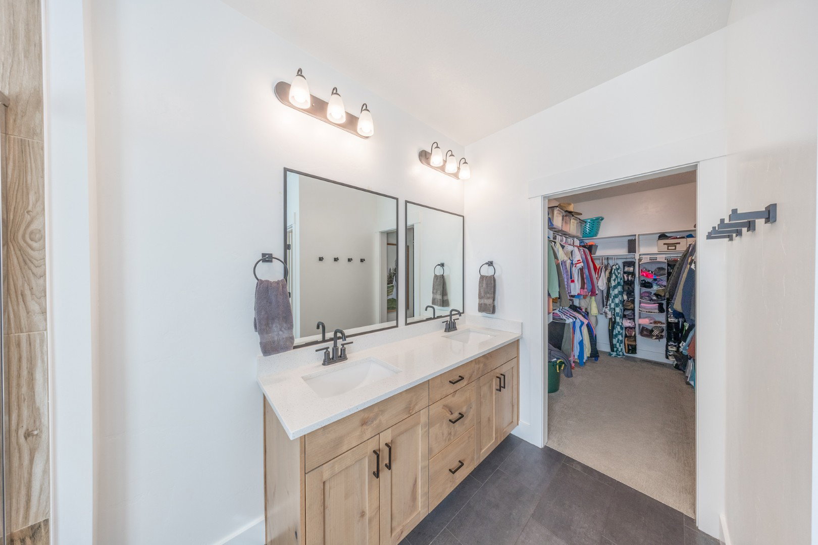 Full bathroom featuring double vanity, a walk in closet, dark colored carpet, and dark tile patterned floors