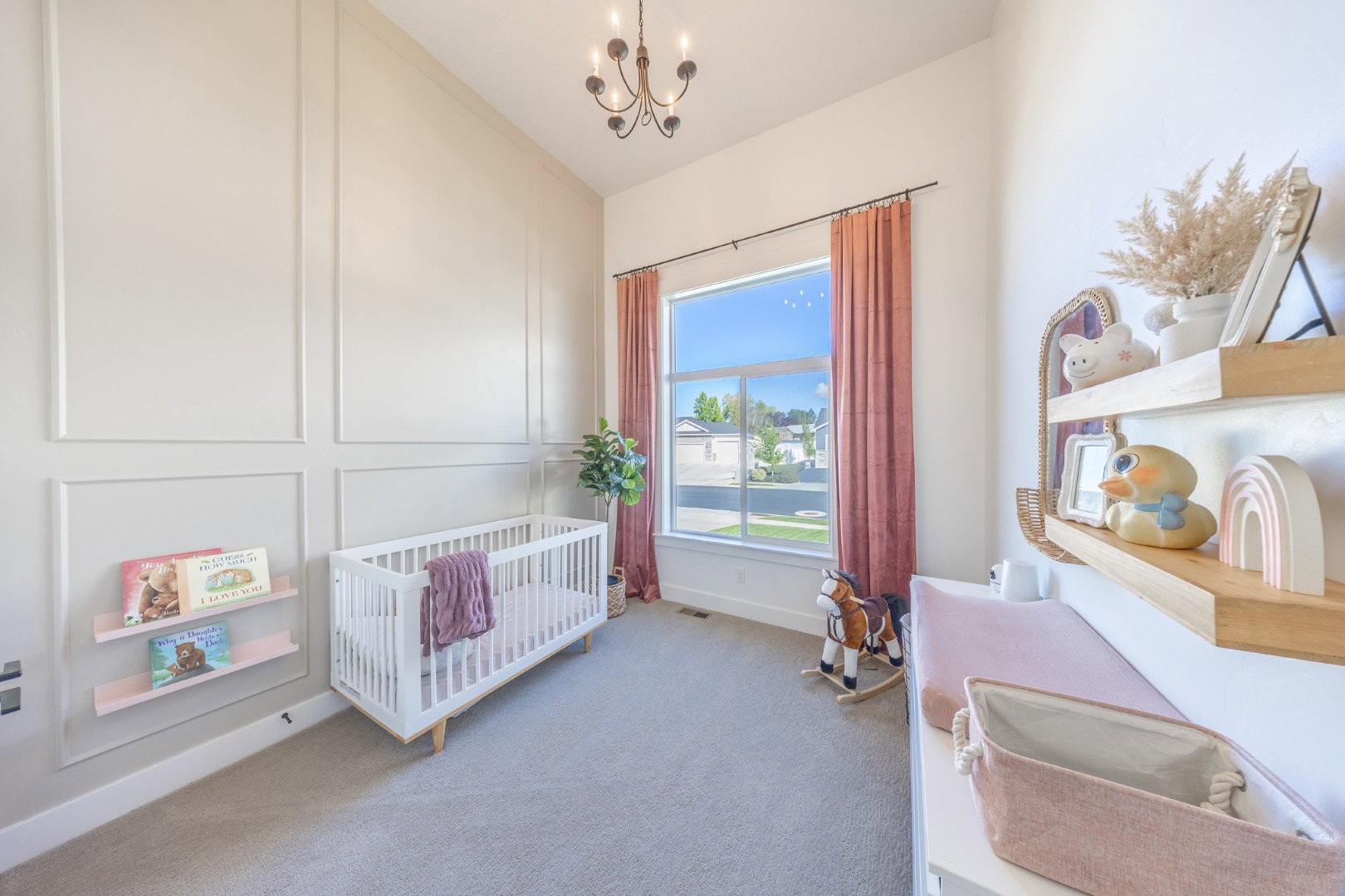 Bedroom featuring a crib, light colored carpet, a chandelier, vaulted ceiling, and a decorative wall