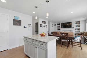 Kitchen featuring a kitchen island, decorative light fixtures, light stone counters, open floor plan, and light wood-type flooring