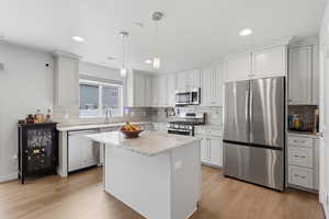 Kitchen with stainless steel appliances, light wood finished floors, light stone counters, and a kitchen island