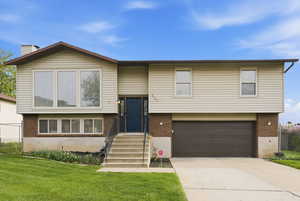 Split foyer home with a garage, brick siding, concrete driveway, and a chimney