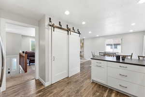 Kitchen with a barn door, white cabinets, dark wood-style floors, dark countertops, and recessed lighting