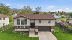 Bi-level home featuring brick siding, a gate, a garage, concrete driveway, and a mountain view
