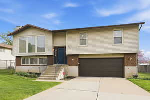 Bi-level home featuring brick siding, an attached garage, a front yard, and driveway