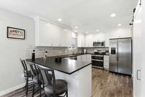 Kitchen with stainless steel appliances, a barn door, dark wood-style floors, white cabinets, and a peninsula