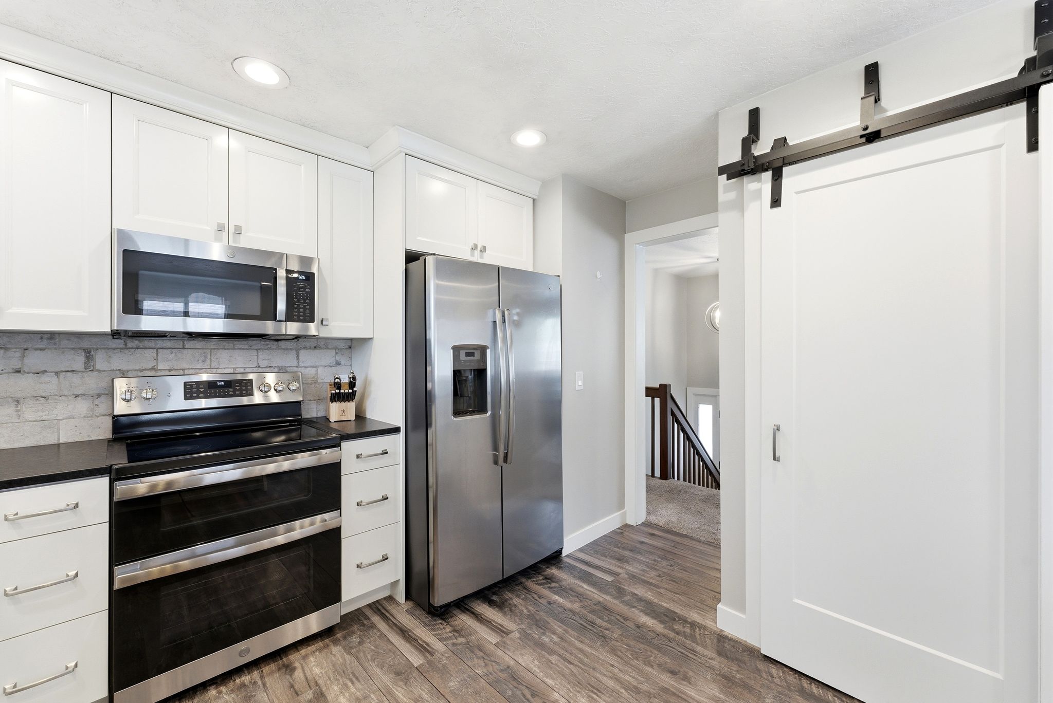 Kitchen featuring stainless steel appliances, a barn door, white cabinetry, dark wood-style flooring, and recessed lighting