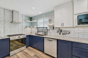 Kitchen with stainless steel appliances, blue cabinetry, light stone counters, light wood-style floors, and recessed lighting
