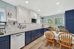 Kitchen featuring open shelves, dishwashing machine, light wood finished floors, two tone cabinetry, and light stone countertops