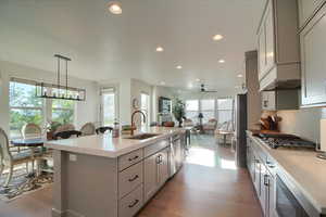 Kitchen featuring an island with sink, light wood finished floors, gray cabinetry, and pendant lighting
