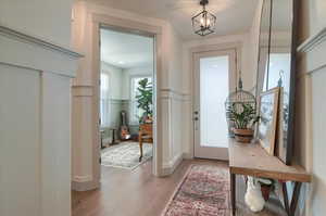 Entrance foyer with light wood finished floors, wainscoting, and suspended lighting