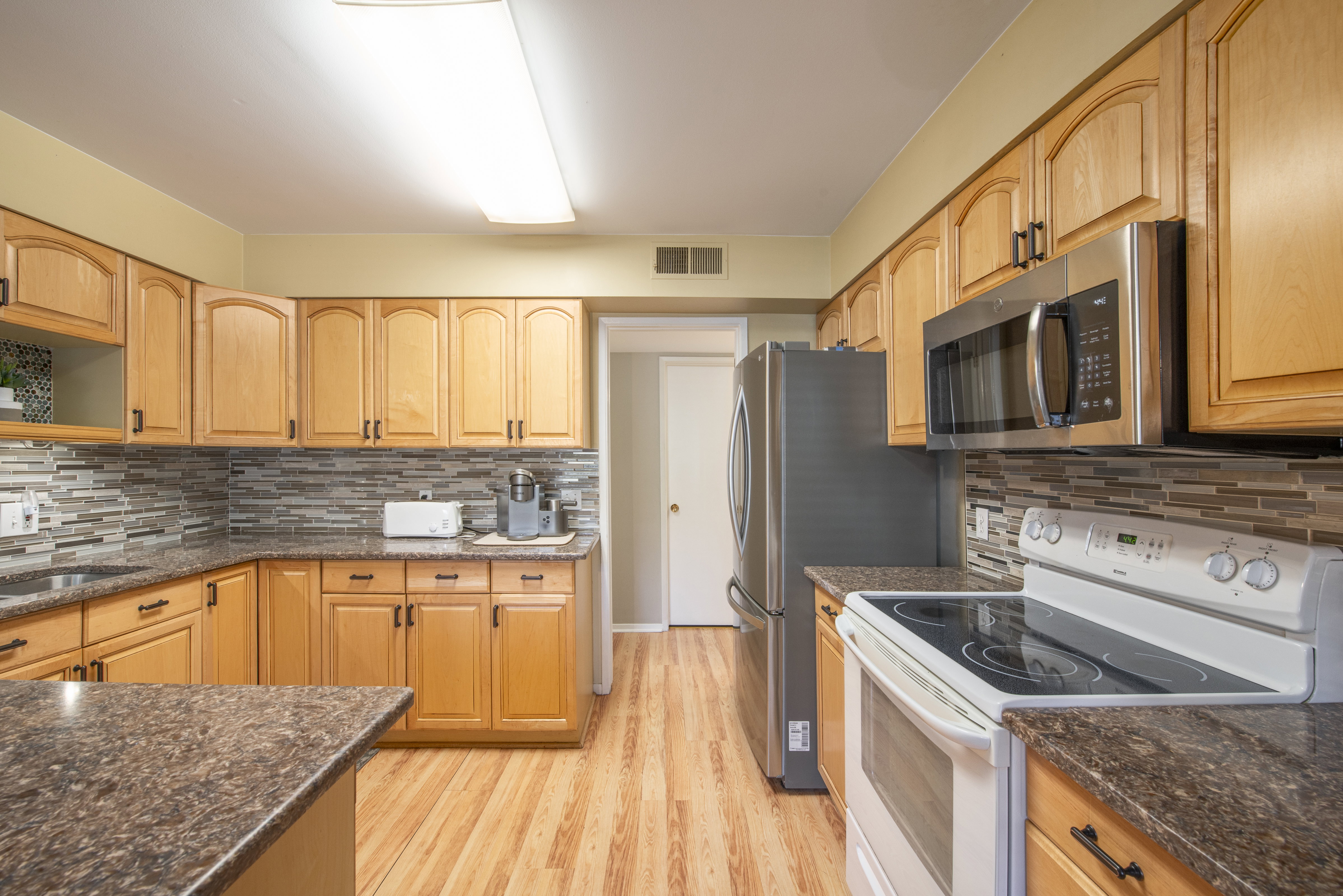 Kitchen with white electric range oven, stainless steel microwave, dark stone counters, light wood finished floors, and decorative backsplash