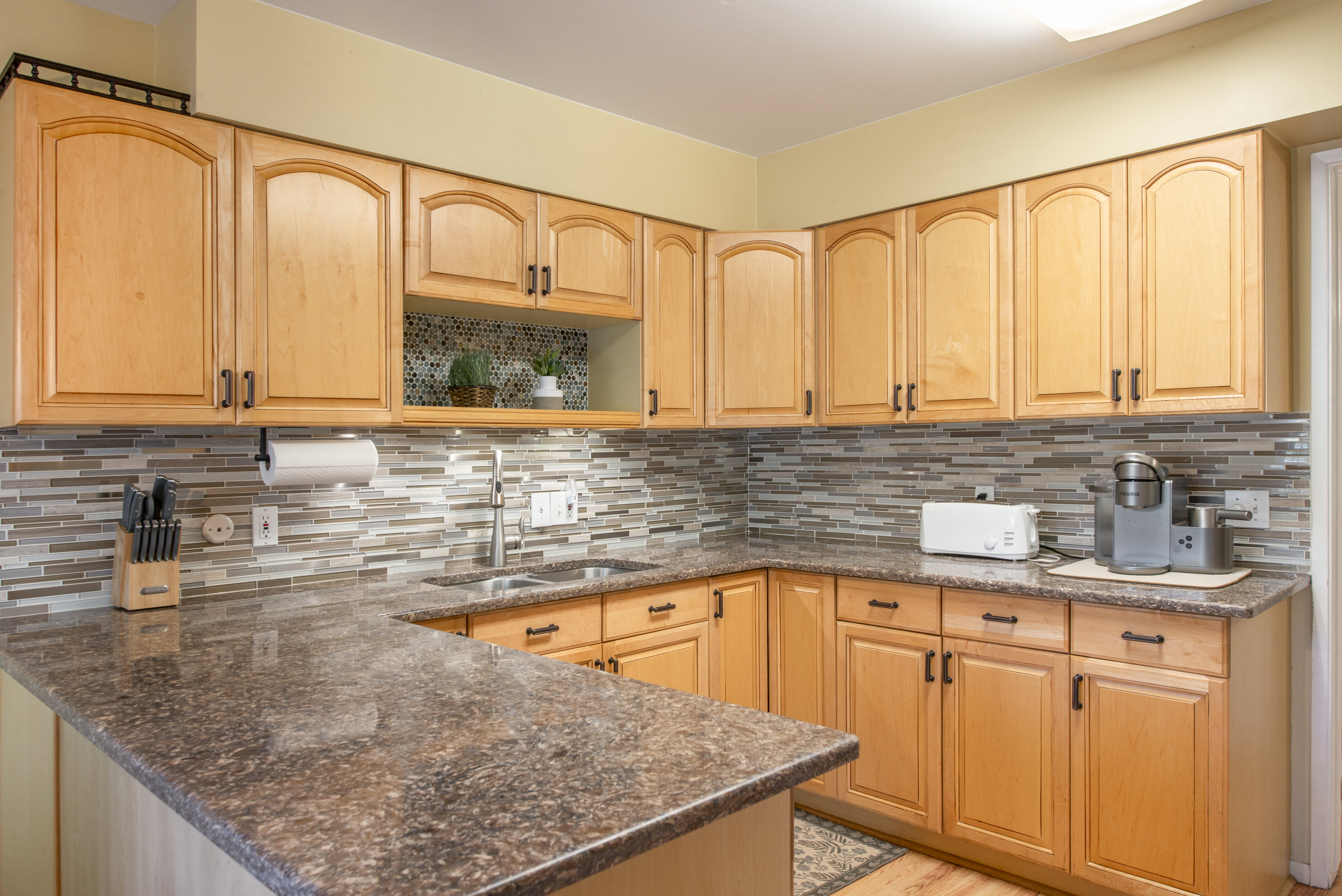 Kitchen with light wood finish cabinetry, dark stone counters, and a peninsula