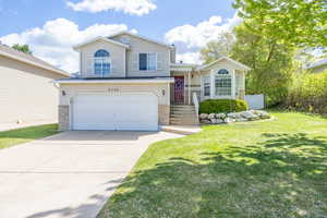Split level home featuring a garage, driveway, a front yard, and stone siding