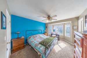 Bedroom with ceiling fan, carpet flooring, and a textured ceiling