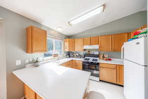 Kitchen featuring freestanding refrigerator, gas range oven, light countertops, vaulted ceiling, and a peninsula