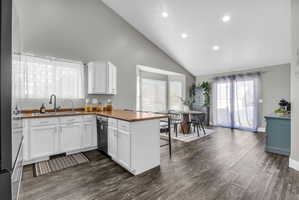 Kitchen with a peninsula, dark wood-style floors, stainless steel appliances, white cabinetry, and vaulted ceiling