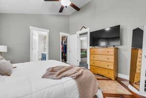 Bedroom with ensuite bathroom, lofted ceiling, a spacious closet, and ceiling fan