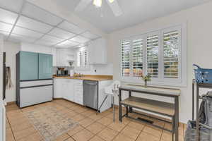 Kitchen with freestanding refrigerator, white cabinetry, dishwasher, light tile patterned floors, and ceiling fan