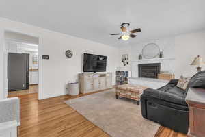 Living room featuring light wood-type flooring, a fireplace, and a ceiling fan