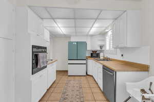Kitchen with white cabinetry, stainless steel appliances, open shelves, and light tile patterned floors