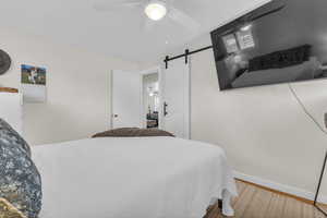 Bedroom featuring a barn door, light wood-style flooring, and ceiling fan