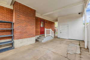 Carport and doorway to property featuring brick. Storage