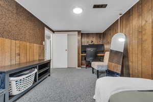 Bedroom with wood walls, carpet floors, and an office area