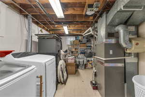 Unfinished below grade area with light flooring, heating unit, and washer and clothes dryer