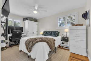 Bedroom with a desk, light wood-style flooring, and ceiling fan