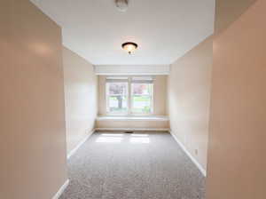Empty room with light colored carpet and a smoke detector