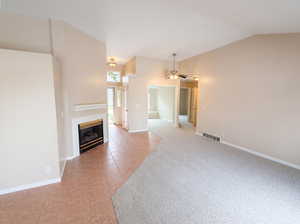 Unfurnished living room featuring a ceiling fan, lofted ceiling, a glass covered fireplace, light colored carpet, and light tile patterned floors