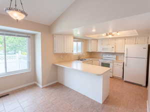 Kitchen featuring light countertops, white appliances, white cabinetry, a peninsula, and vaulted ceiling