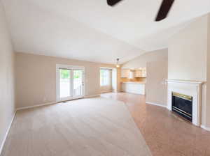 Unfurnished living room featuring ceiling fan, vaulted ceiling, a glass covered fireplace, and light tile patterned flooring