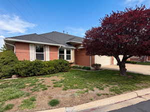 View of front facade featuring brick siding, a garage, concrete driveway, a front yard, and roof with shingles
