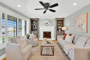 Living area with a ceiling fan, a fireplace with raised hearth, built in features, recessed lighting, and wood finished floors