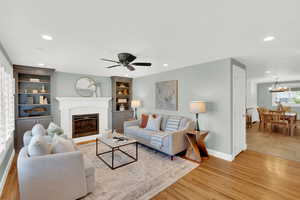 Living area featuring light wood-style floors, a glass covered fireplace, built in features, recessed lighting, and ceiling fan