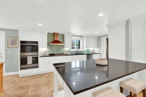 Kitchen featuring a breakfast bar, stainless steel appliances, white cabinets, tasteful backsplash, and dark stone counters