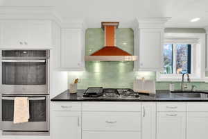Kitchen with stainless steel appliances, exhaust hood, dark stone counters, and white cabinets